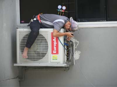 HVAC technician performing repair work on a wall-mounted outdoor air conditioning unit.