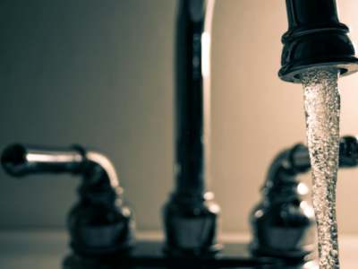 Close-up of water streaming from a chrome faucet with blurred handles in the background.