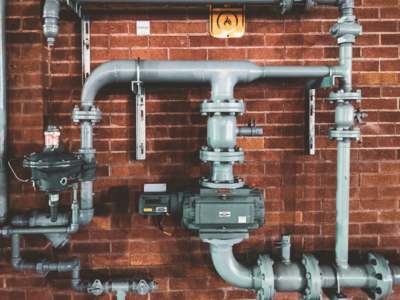 Gas piping system with valves, regulators, and a meter mounted on a red brick wall.