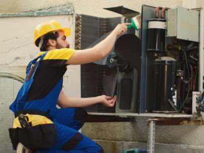 HVAC technician inspecting outdoor air conditioning condenser unit during routine maintenance.