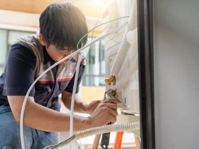 Technician performing maintenance inspection on residential Carrier heat pump system using a flashlight for diagnostic check.