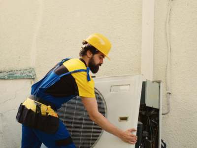 Professional HVAC technician in uniform servicing a residential air conditioning unit.