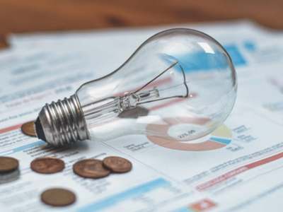 Clear incandescent light bulb and copper coins resting on financial documents with charts.