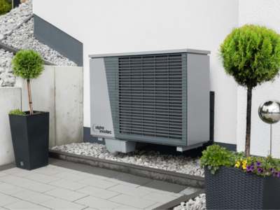 Modern gray heat pump unit installed on white gravel bed in landscaped patio area.