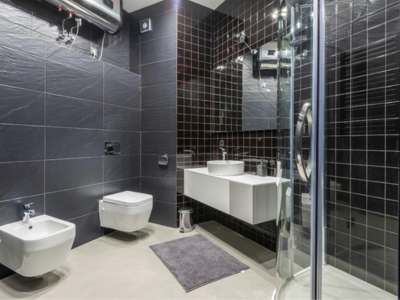 Stainless steel wall-mounted water heater with exposed pipes in a bathroom.