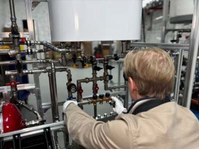 Technician in beige jacket adjusting valves on complex piping system.