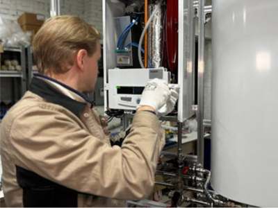 Technician in a tan uniform servicing an open wall-mounted tankless water heater unit.