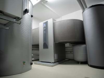 Utility room with a heat pump unit, large insulated storage tanks, and connected piping in a clean installation.